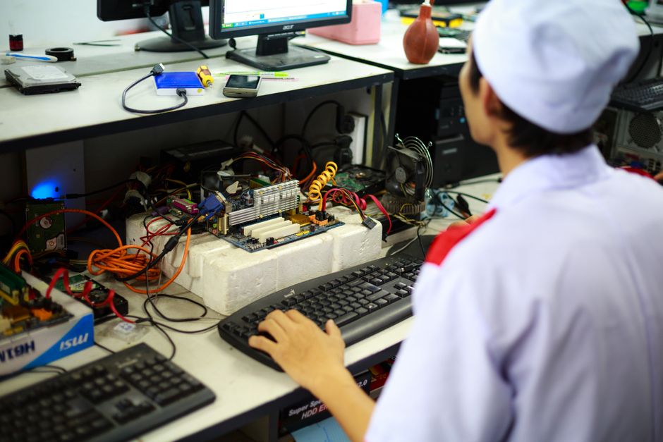 A technician in uniform working on a motherboard at a desk in a laboratory setting.